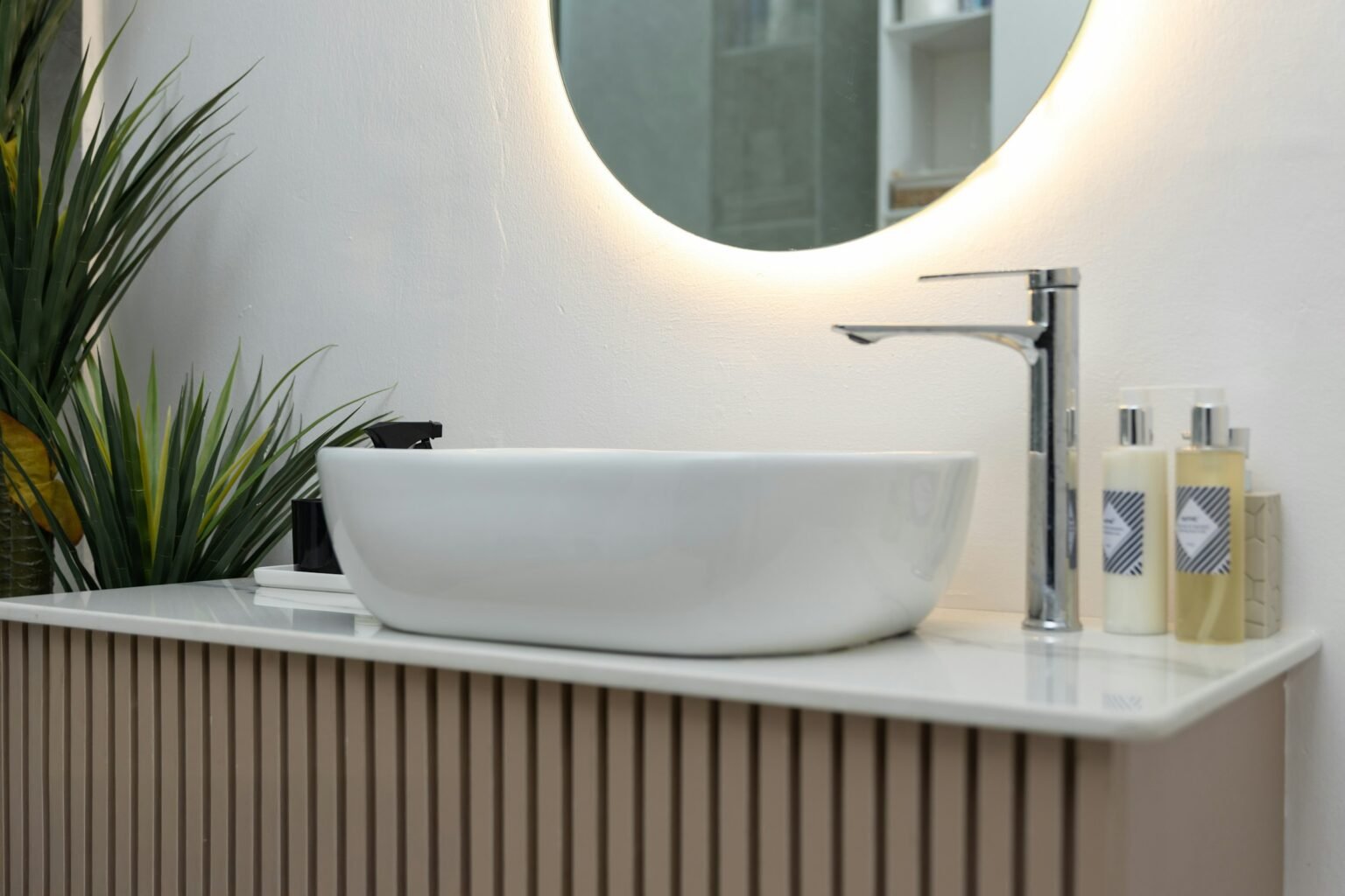 Backlit vs front lit mirror: a round backlit mirror glowing above a white vessel sink and wood vanity