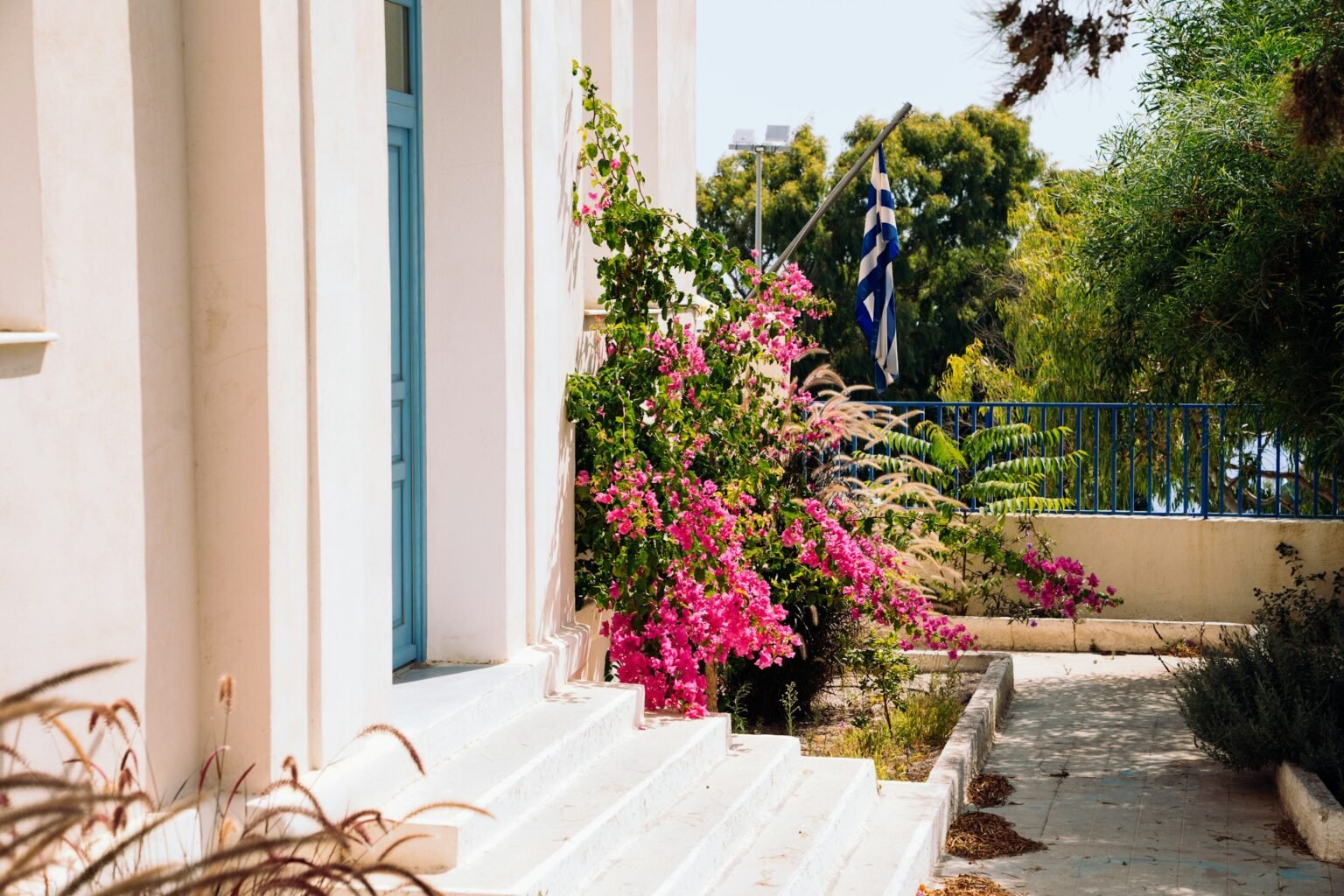 Artificial bougainvillea inspiration: bright blooms spilling beside white front steps and a blue door