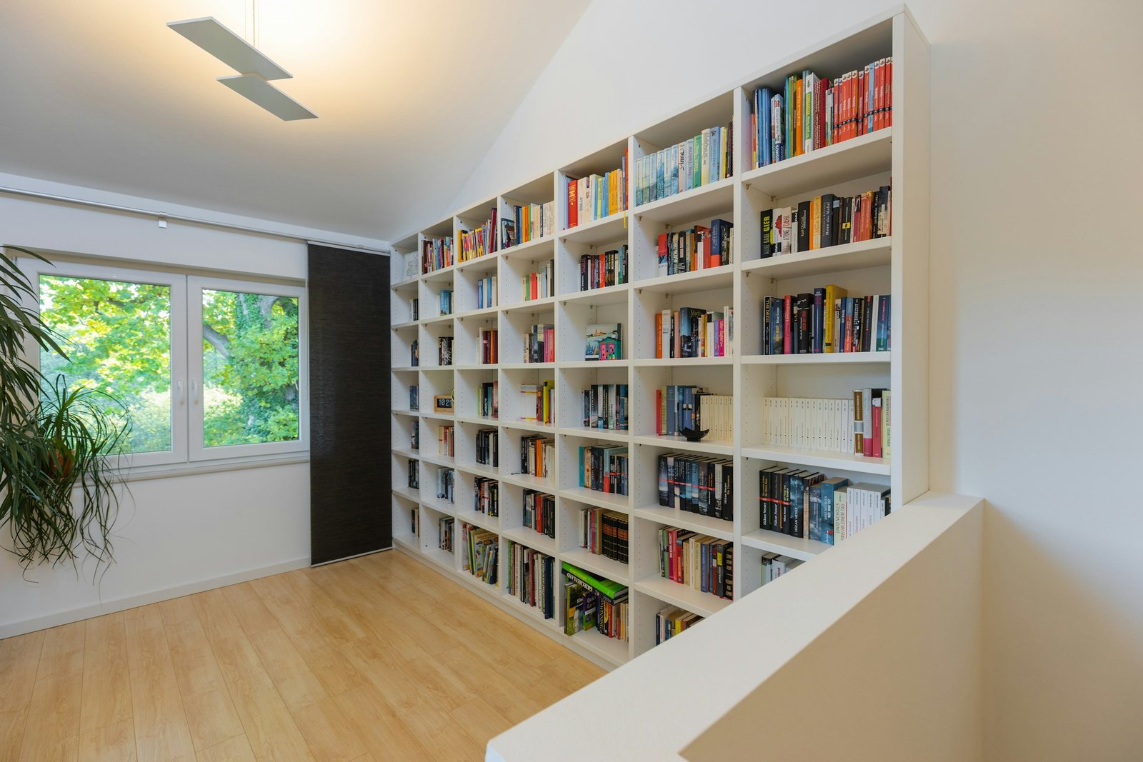 Tall white bookshelves for heavy books lining a bright home office wall