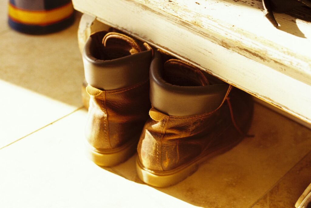 Worn leather boots under an entryway bench in a sunlit hallway, a spot where a boot tray for entryway use keeps floors dry