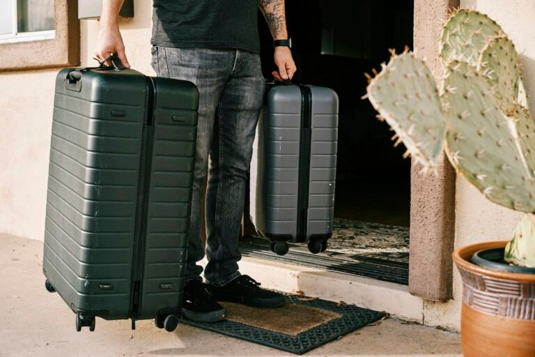 Best carry on luggage size check: a traveler holds a large checked suitcase next to a smaller carry-on spinner at the front door