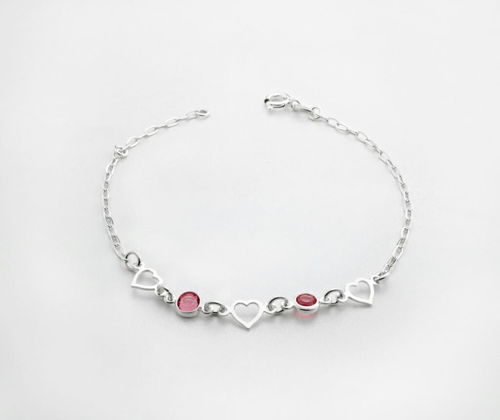 Silver charm bracelet for women with open heart links and pink stones on a white background