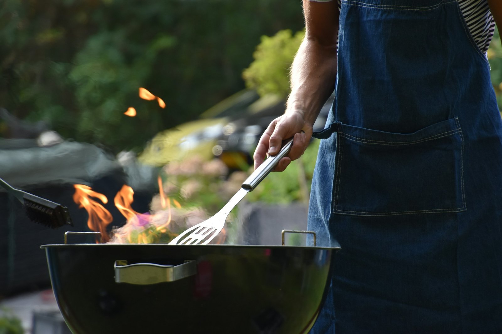 Christmas gifts for dads who like to grill: a man in a denim apron flipping food on a charcoal grill