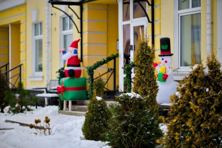 Best Christmas inflatables in a snowy front yard: an inflatable Santa with a gift box and an inflatable snowman by the entry