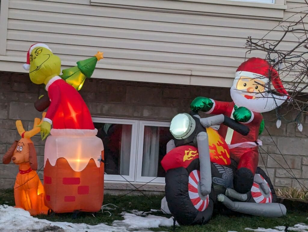 Outdoor Christmas inflatables tethered on a front lawn, a lit chimney character scene and Santa on a motorcycle