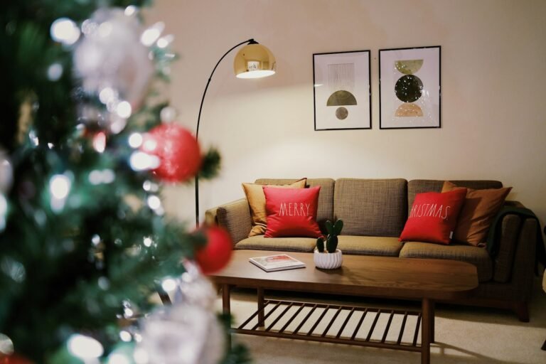 Christmas pillow covers in red on a gray sofa beside a lit Christmas tree in a cozy living room