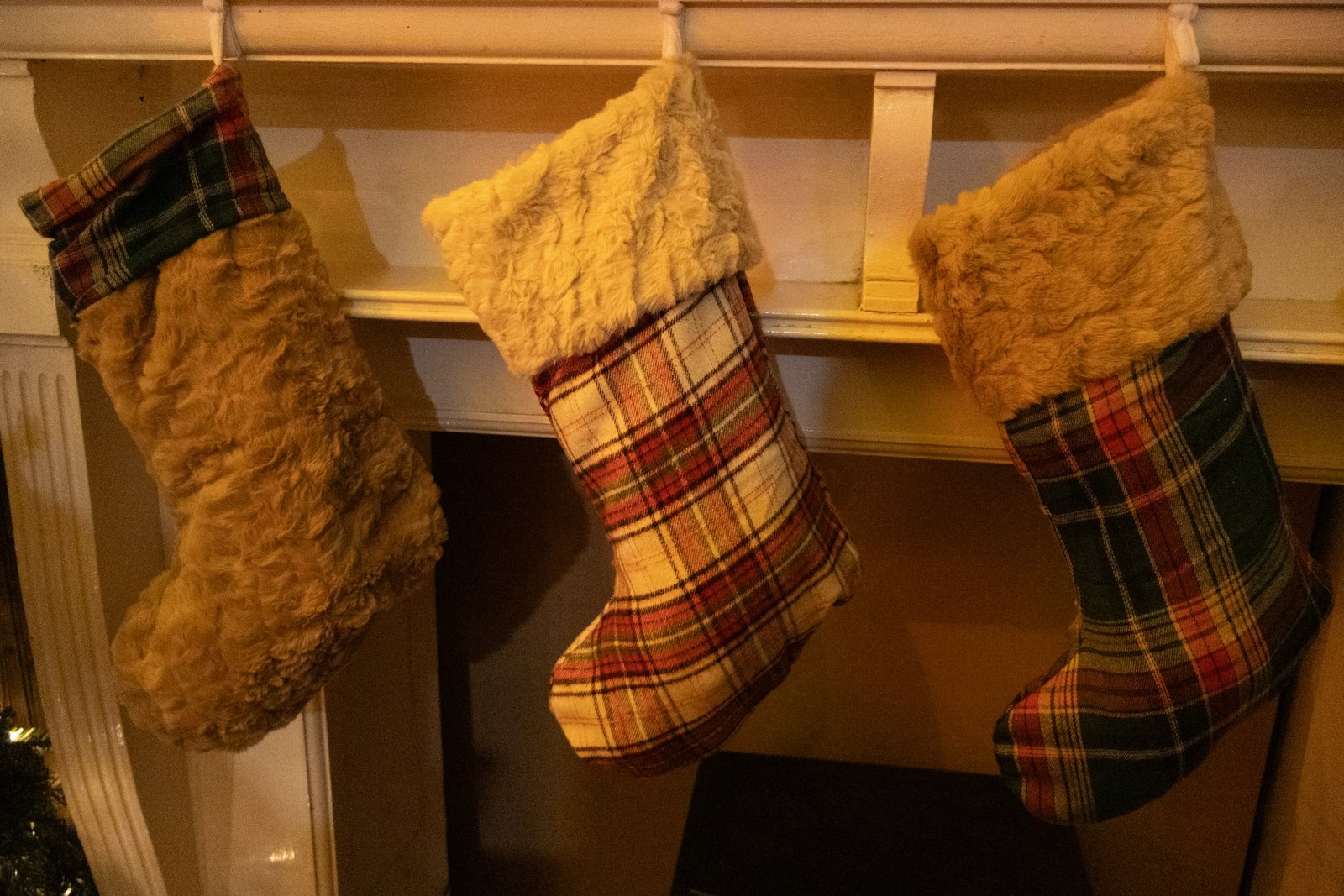 Plaid and faux fur stockings hung from stocking holders for mantel on a white fireplace