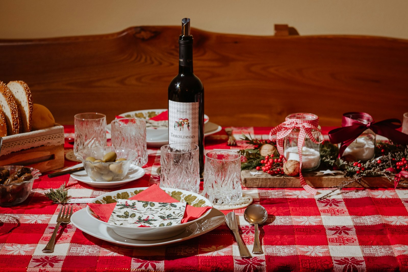 Christmas tablecloth idea: red and white check holiday table linen set with white plates, crystal glasses, holly berries and red wine