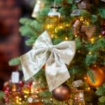 Best christmas tree ribbon idea: a champagne velvet bow on a lit Christmas tree with gold and burgundy ornaments