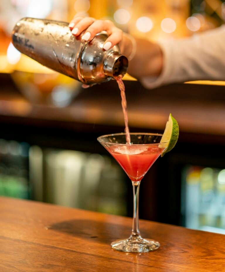 Cocktail shaker set for beginners in action: a cobbler shaker pours a pink cocktail into a martini glass