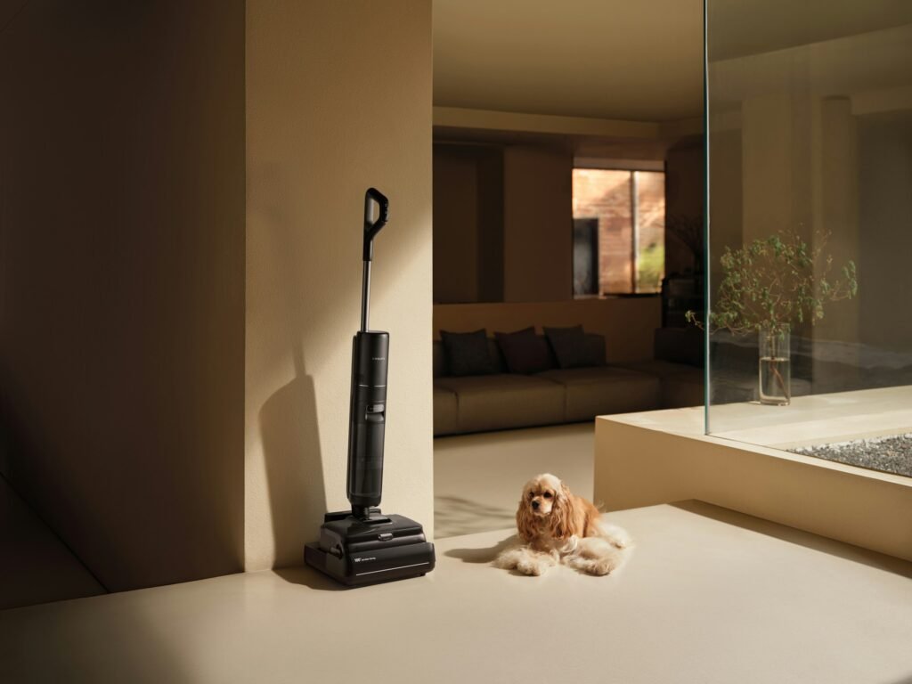 Best cordless vacuum for pet hair: a cordless stick vacuum standing on its charging base next to a fluffy dog in a modern living room