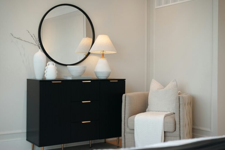 Best dressers: a black 6-drawer dresser with brass pulls, a round mirror and a lamp in a bright bedroom