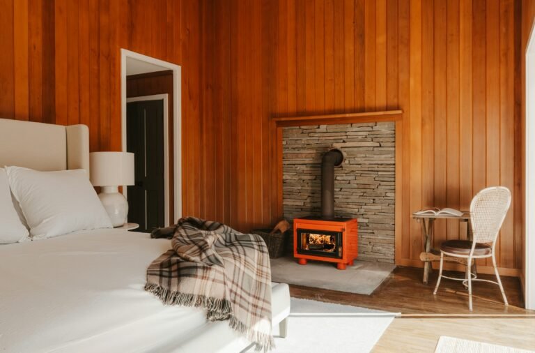 Best flannel sheets for a cozy winter bedroom: white bed with a plaid wool throw beside a wood stove in a cedar-paneled room
