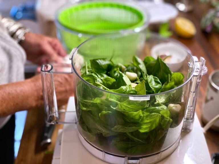 Best food processor in use: fresh basil and garlic in a clear work bowl for homemade pesto