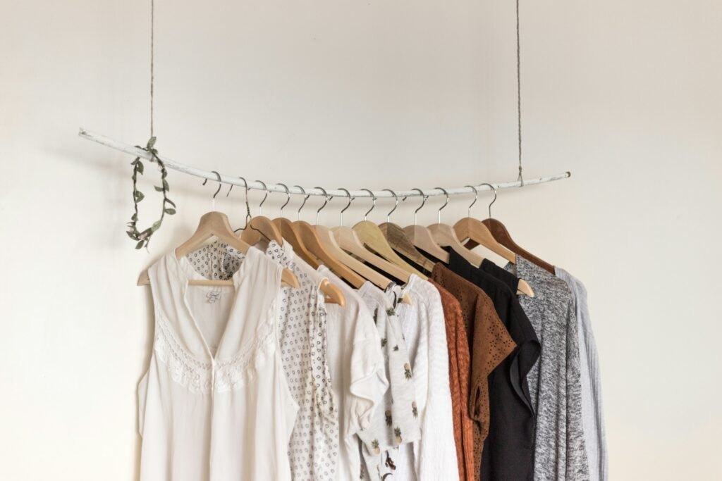 Open clothes rail with neutral shirts and dresses on wooden hangers in a bright minimalist bedroom