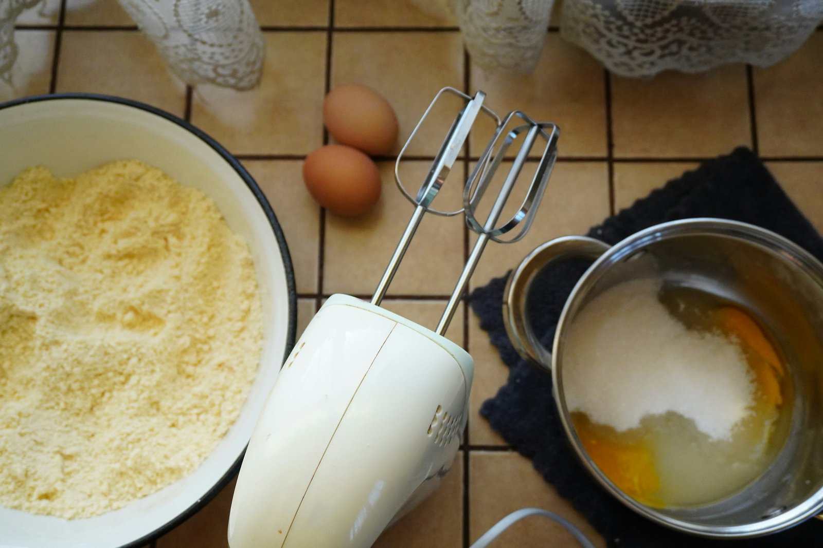 Best hand mixer for baking next to a bowl of flour, eggs and sugar on a kitchen counter