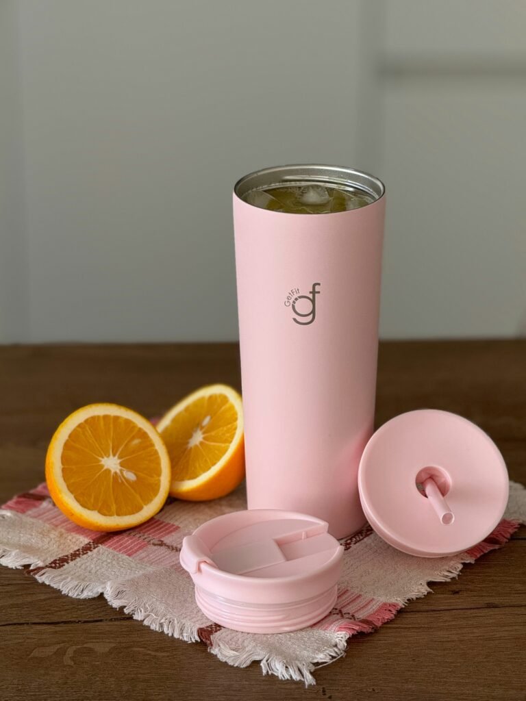 Insulated tumbler with straw lid and spare flip lid next to sliced oranges on a wooden table