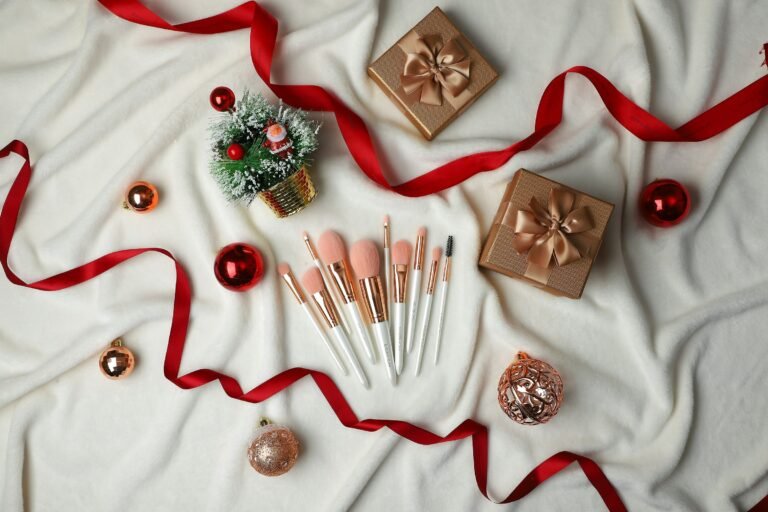 Luxury beauty advent calendar gift idea: makeup brushes, gold gift boxes and red ribbon on a white throw