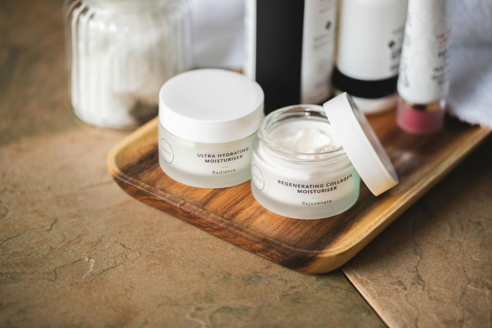 Best luxury body lotion: two white moisturizer jars, one open to show a rich cream, on a wooden tray