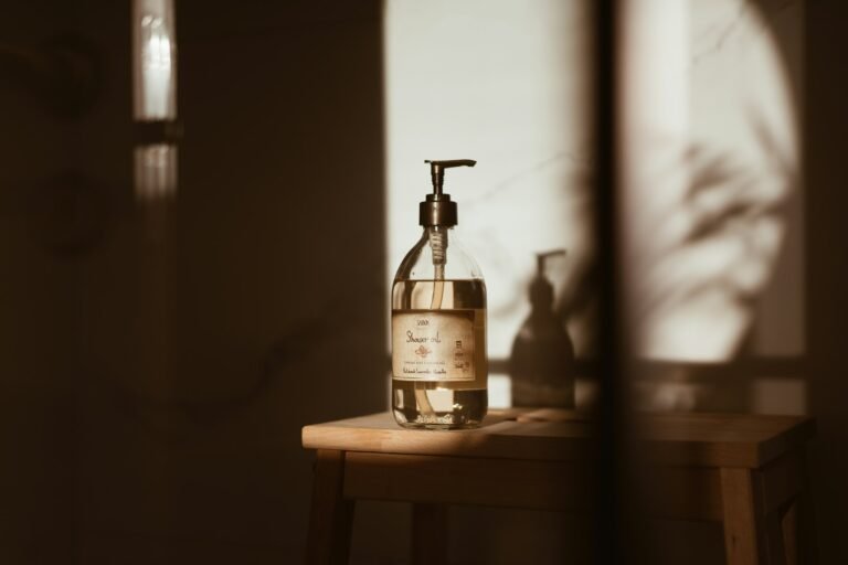 Best luxury body wash: an amber glass pump bottle on a wooden stool in soft window light in a calm bathroom