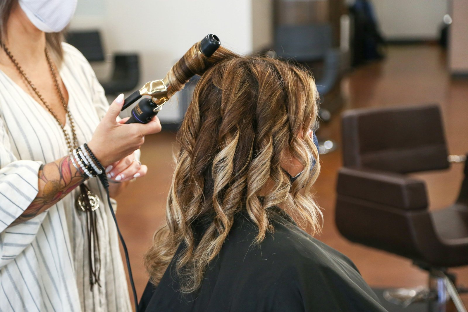 Best luxury curling iron: a stylist curling long highlighted hair with a curling iron in a salon