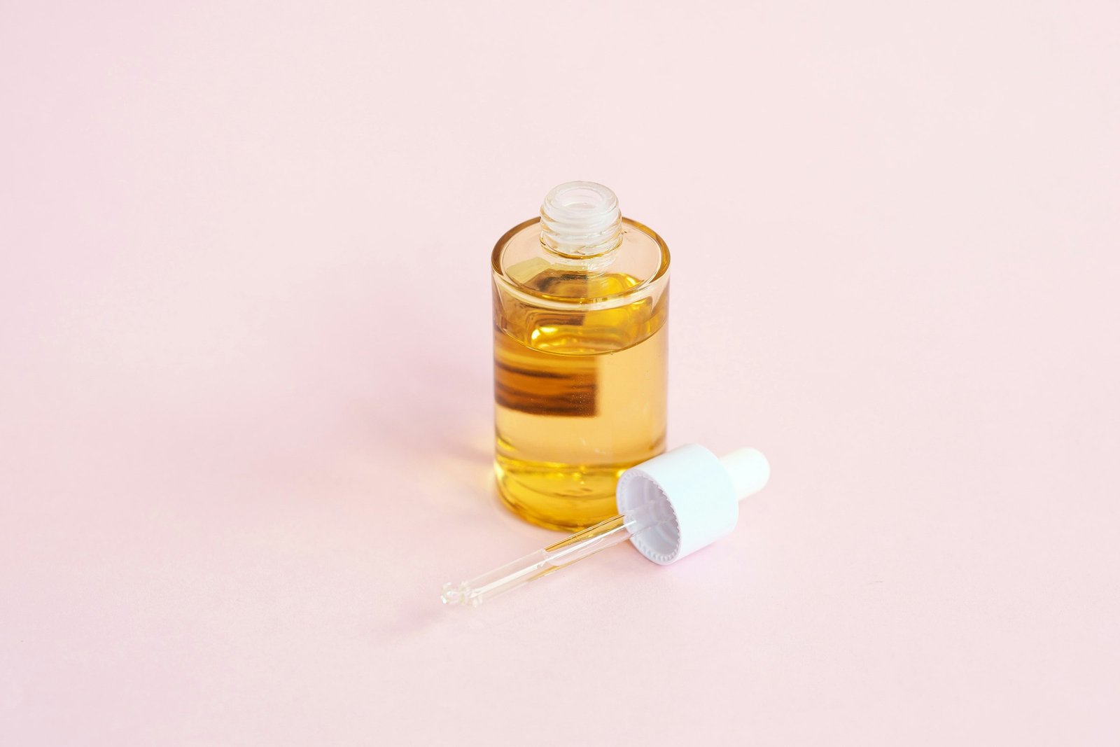 Best luxury serum for sensitive skin routine: a glass serum bottle with its dropper on a soft pink surface