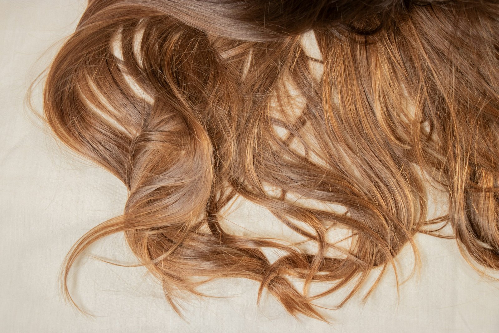 Best luxury hair mask results: long, glossy, soft waves of brown hair spread on a light sheet