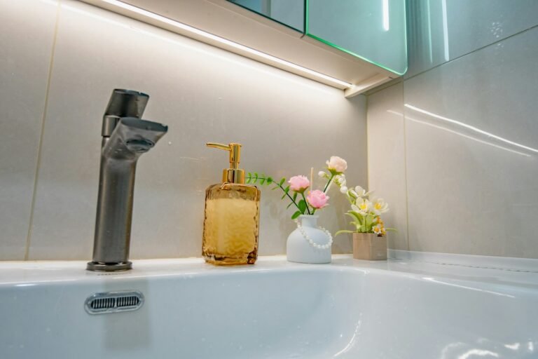 Best luxury hand soap: an amber glass soap pump beside a modern faucet with small pink flowers on a white bathroom sink