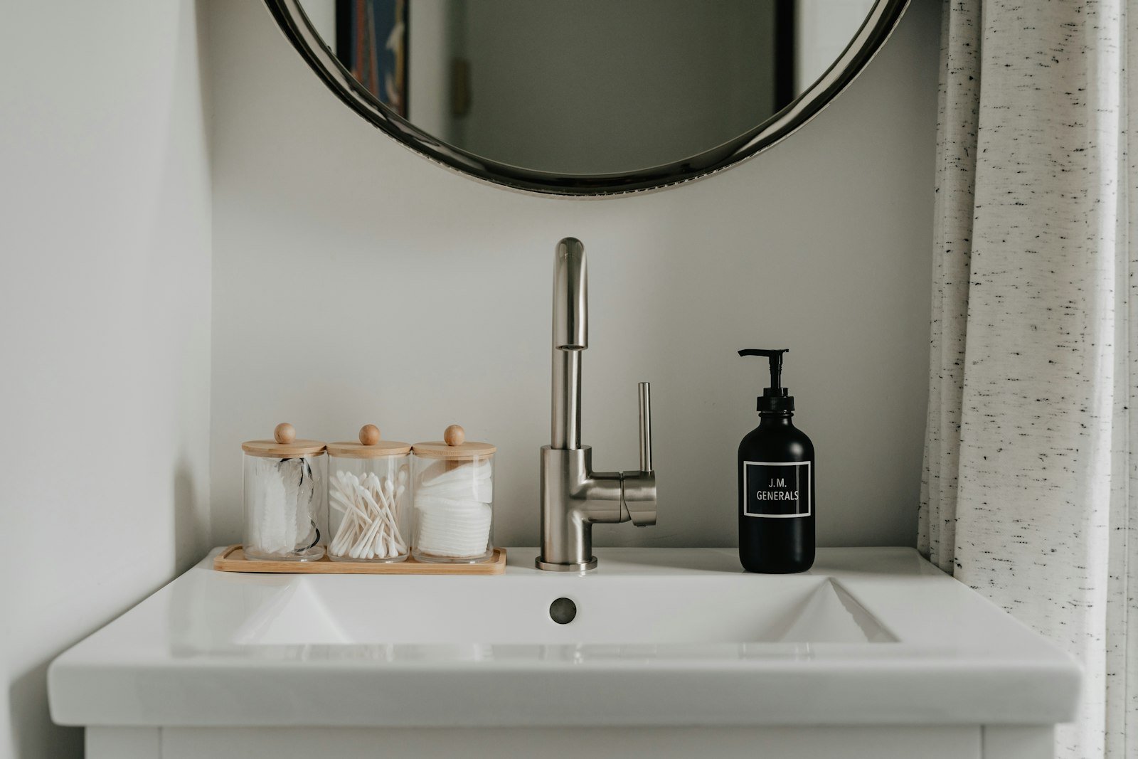 Luxury hand soap for guest bathroom: a dark pump bottle and a wooden tray of glass jars on a white pedestal sink