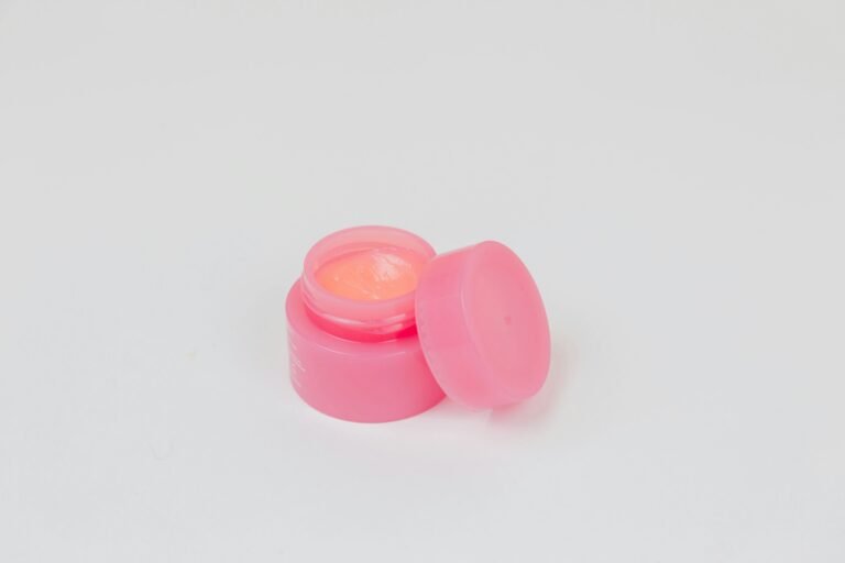 Luxury lip balm: an open pink jar of overnight lip mask with its lid beside it on a white table
