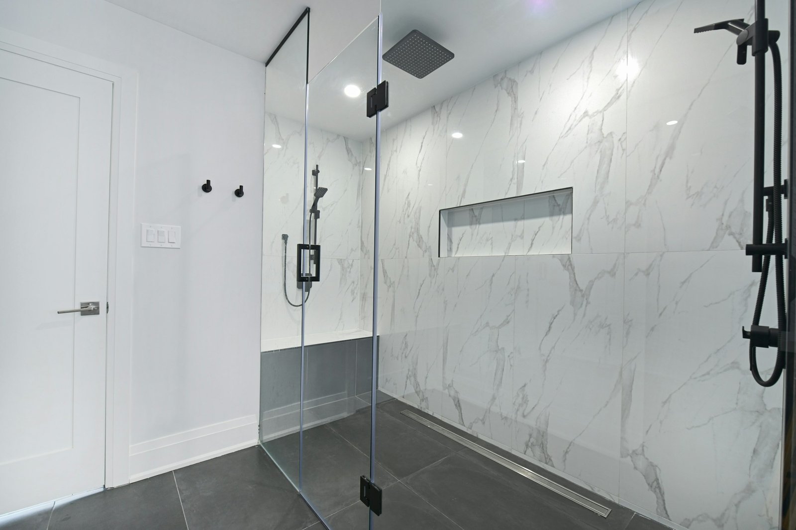 Luxury shampoo and conditioner shelf idea: a walk-in glass shower with marble walls and a long built-in niche