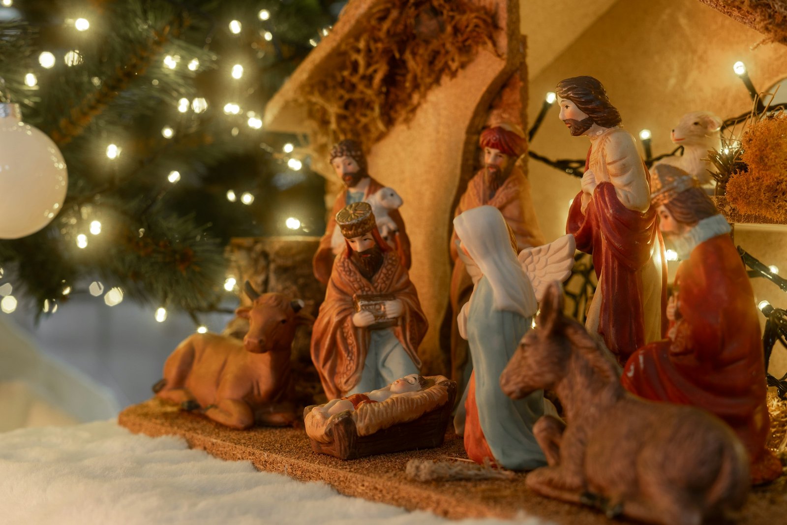 Best nativity sets for Christmas: a painted indoor nativity scene with a stable, wise men and animals beside a lit Christmas tree