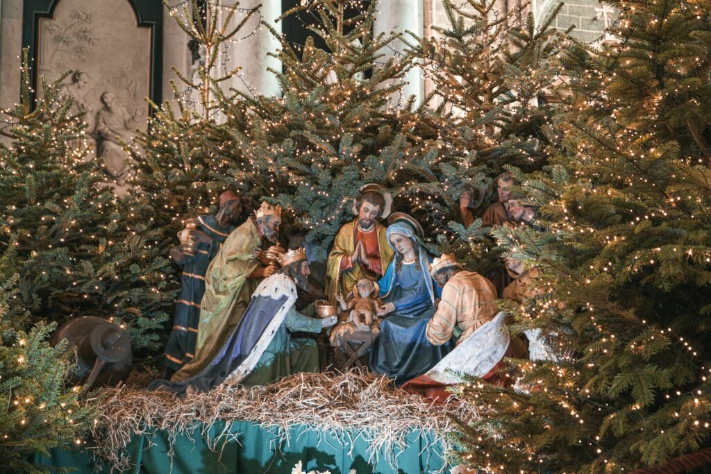 Outdoor nativity set display with life-size figures, straw and lighted evergreen trees