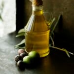 Best olive oil dispenser: a glass cruet of olive oil with a cork stopper beside fresh olives