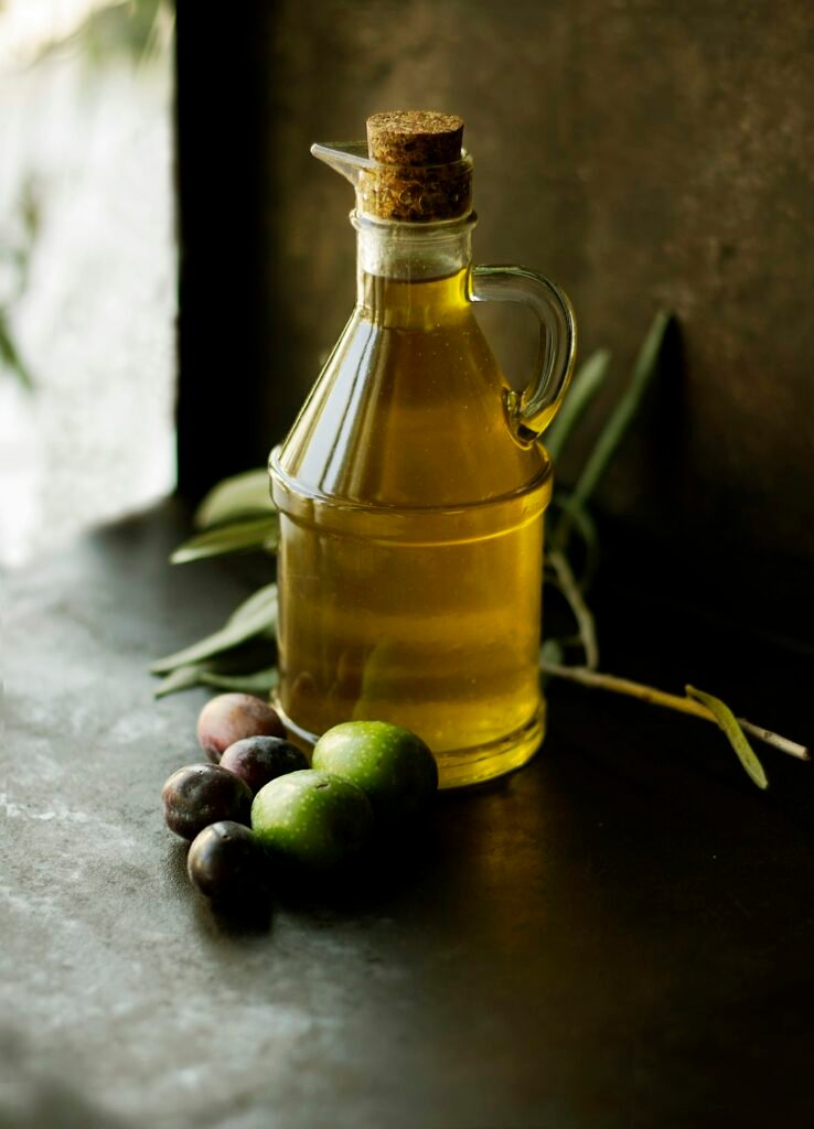 Best olive oil dispenser: a glass cruet of olive oil with a cork stopper beside fresh olives