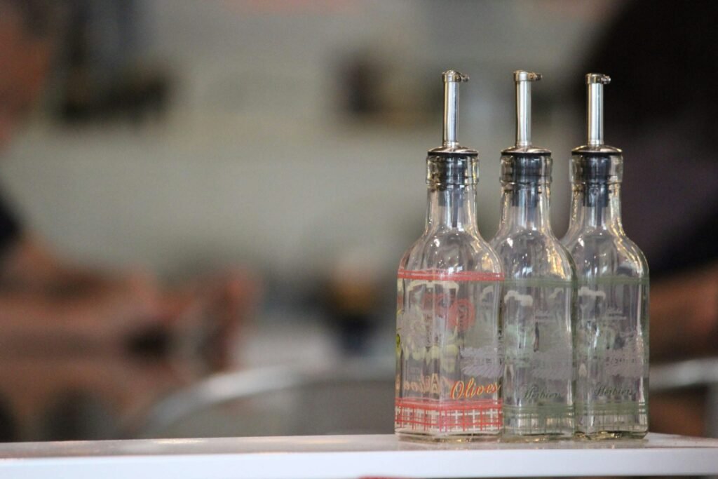 Glass oil dispenser for kitchen: three glass bottles with stainless steel pour spouts on a counter