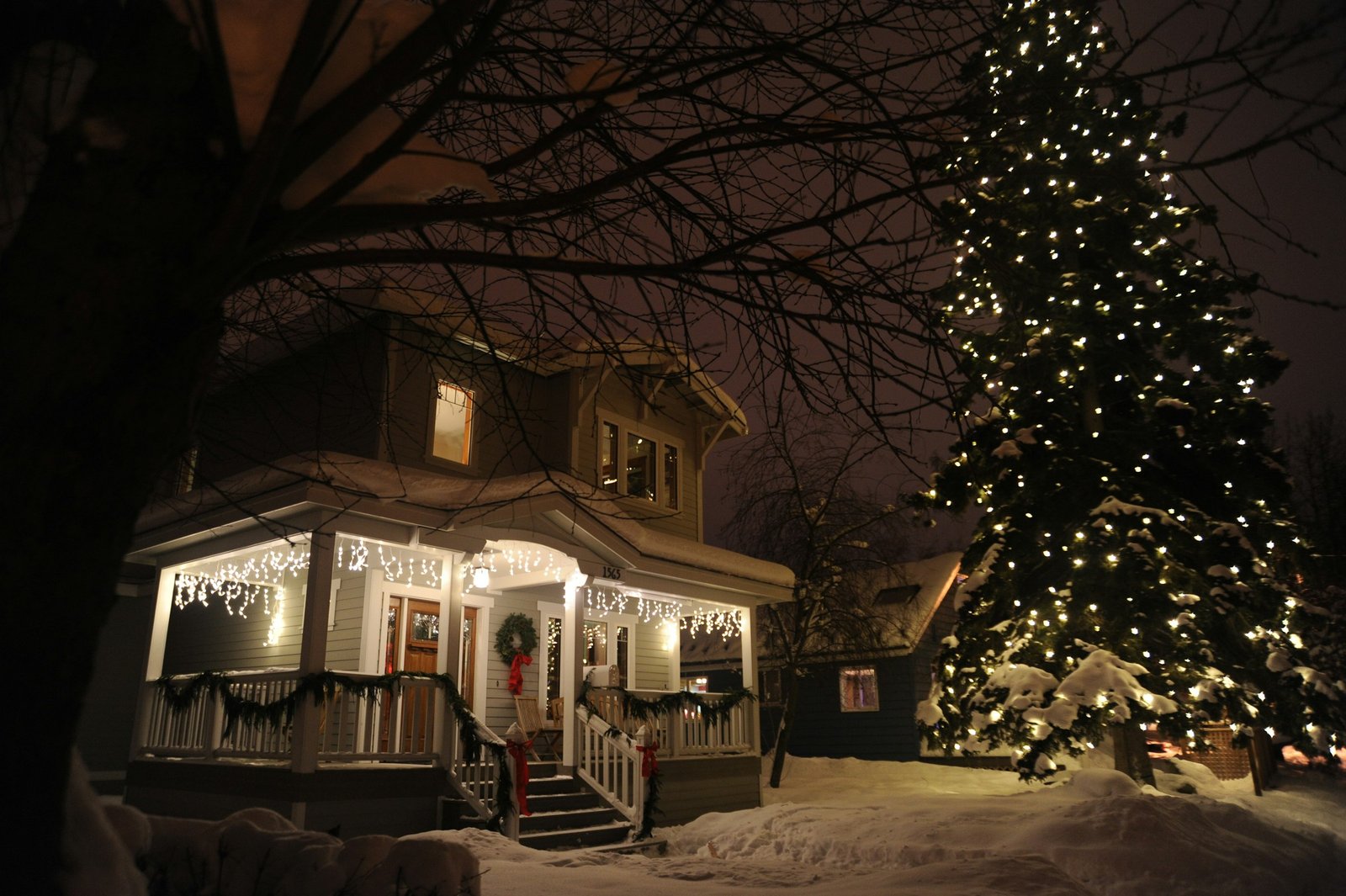 Outdoor timer for Christmas lights: a snowy front porch with white icicle lights and a lit evergreen tree at night