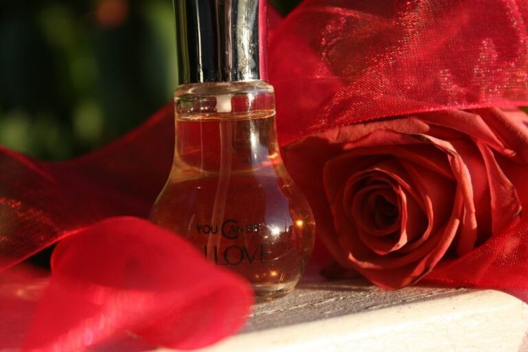 Perfume gift sets for women: a small glass perfume bottle beside a red rose and red organza ribbon