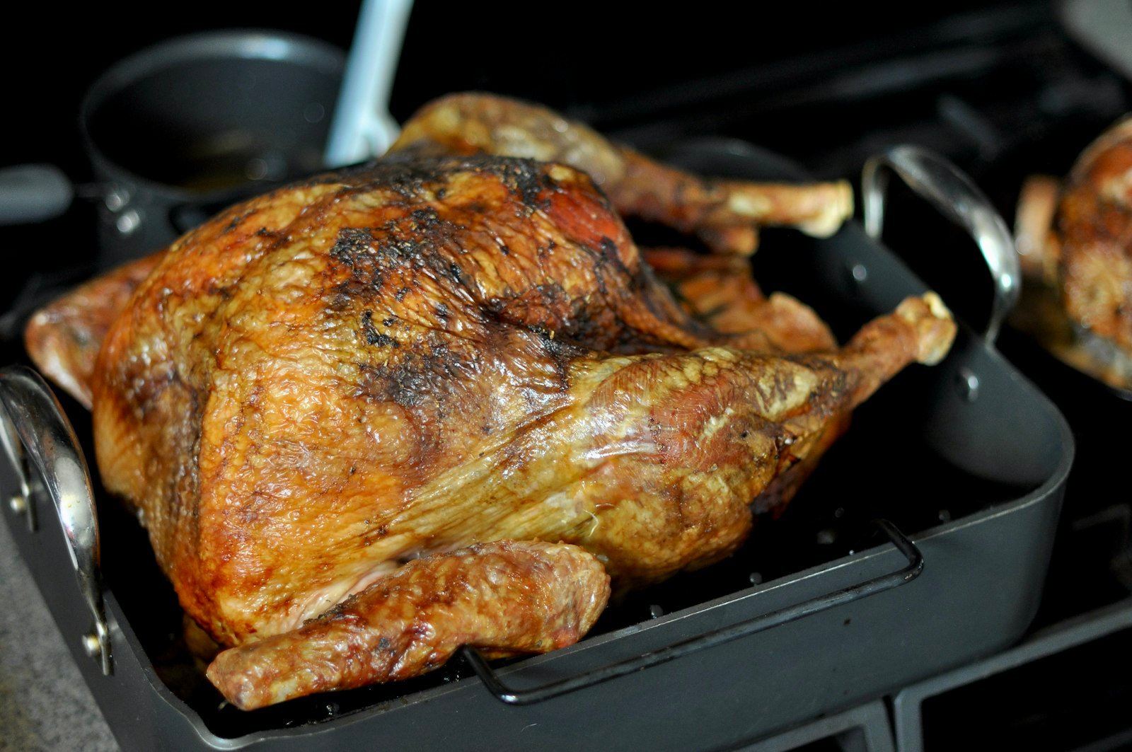 Best roasting pan for turkey: a golden roast turkey on a rack in a dark roasting pan with tall handles