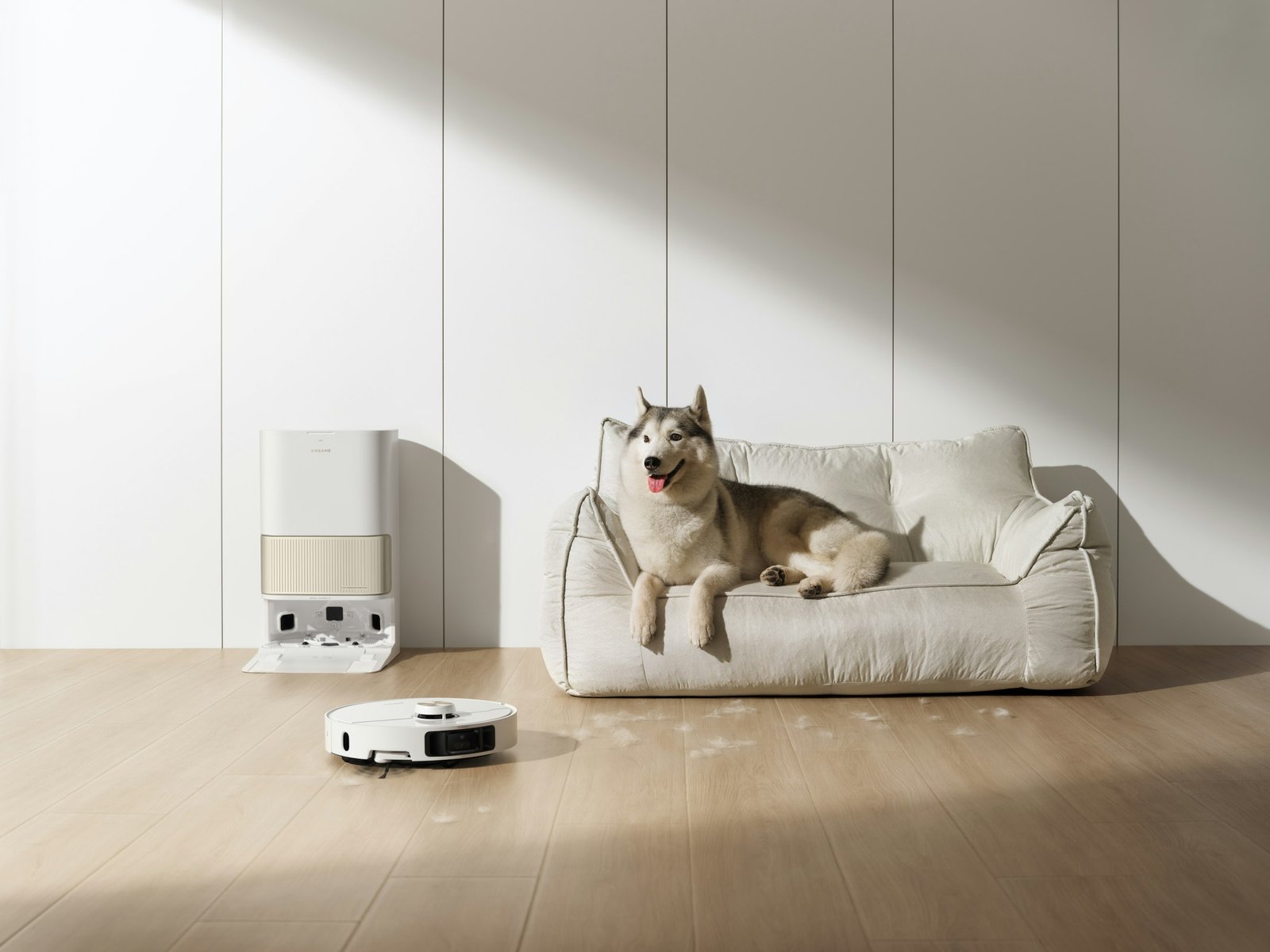 Best robot vacuum for pet hair: a white robot vacuum leaves its self-emptying dock while a husky rests on a light sofa