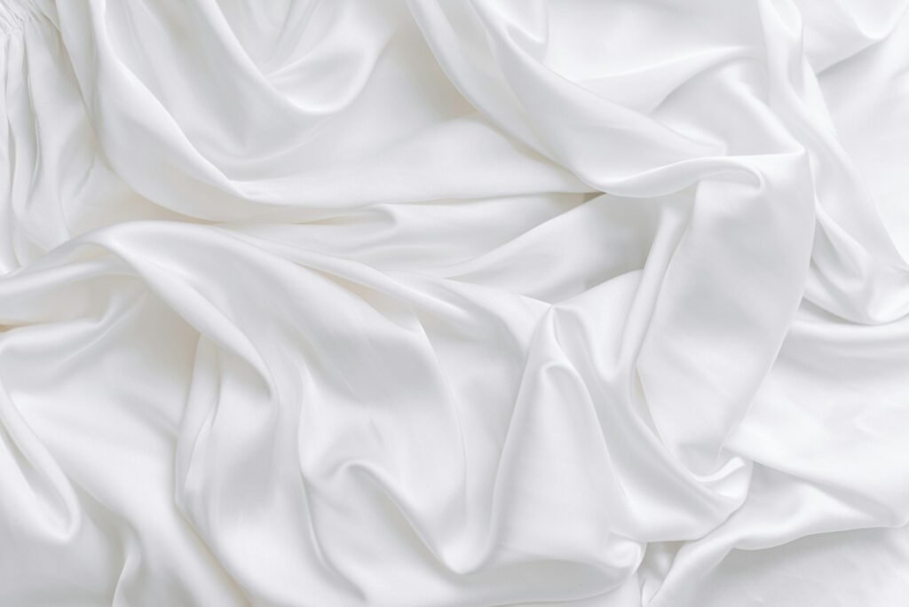 Silk vs satin pillowcase fabric close-up: soft folds of white charmeuse with a smooth, light-catching sheen