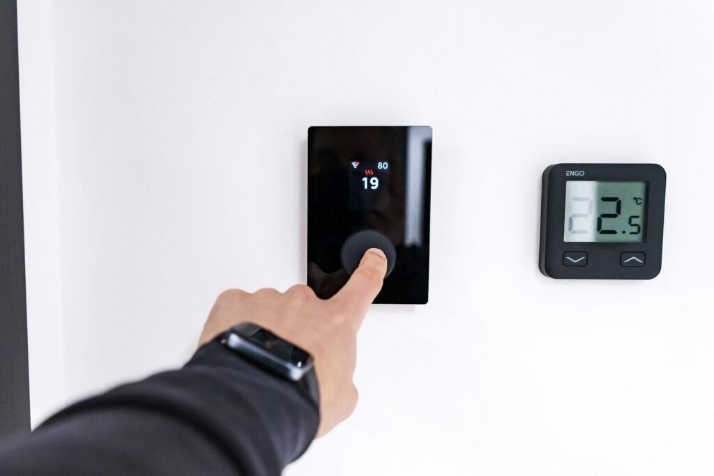 Smart thermostat without C wire installation check: a hand adjusting a modern touch thermostat next to an older digital thermostat