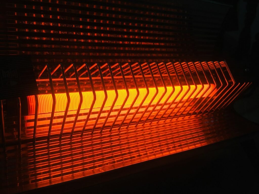 Energy efficient space heater glowing orange behind its safety grille in a dark room