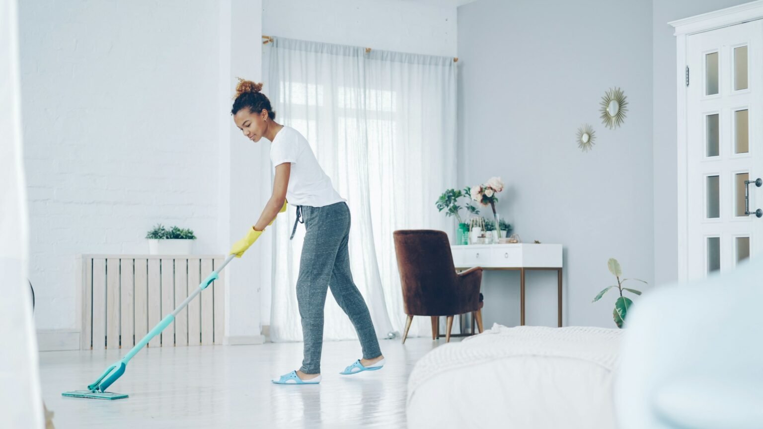 Best steam mop for sealed hard floors: a woman mopping a bright white floor in a sunny living room
