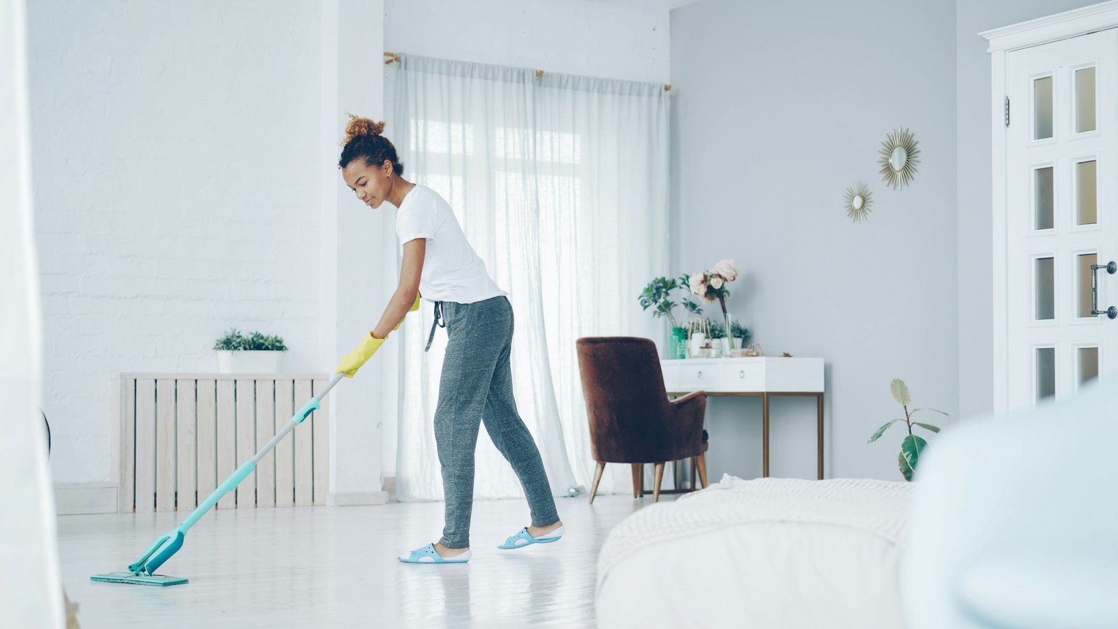 Best steam mop for sealed hard floors: a woman mopping a bright white floor in a sunny living room