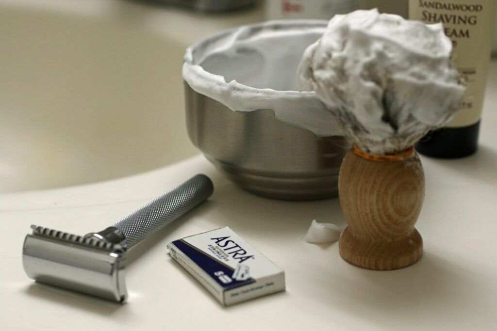 Safety razor, shaving cream and brush on a bathroom counter, ready to pack in the best toiletry bag for men travel kit
