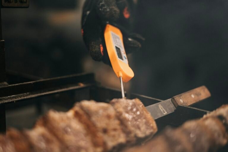 Best wireless meat thermometer alternative: a cook checks grilled meat with a digital probe thermometer over a hot grill