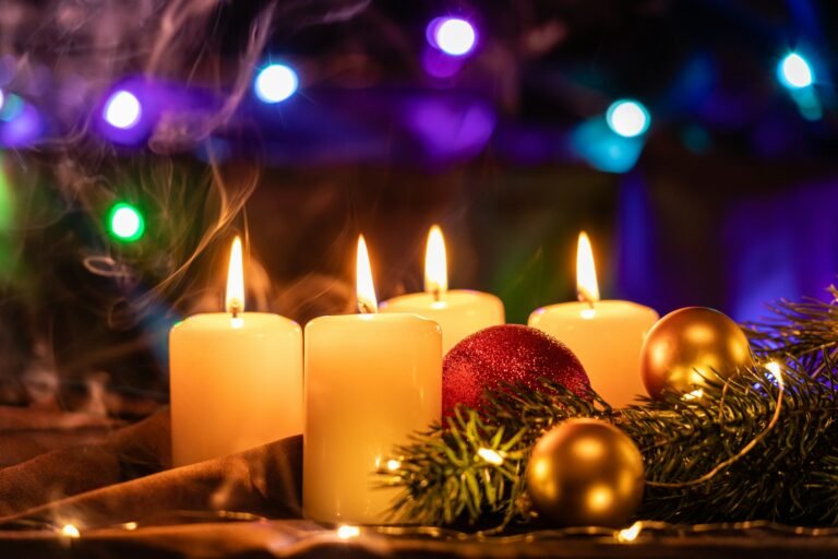 Candle gift ideas: lit ivory pillar candles with gold ornaments and pine on a holiday table