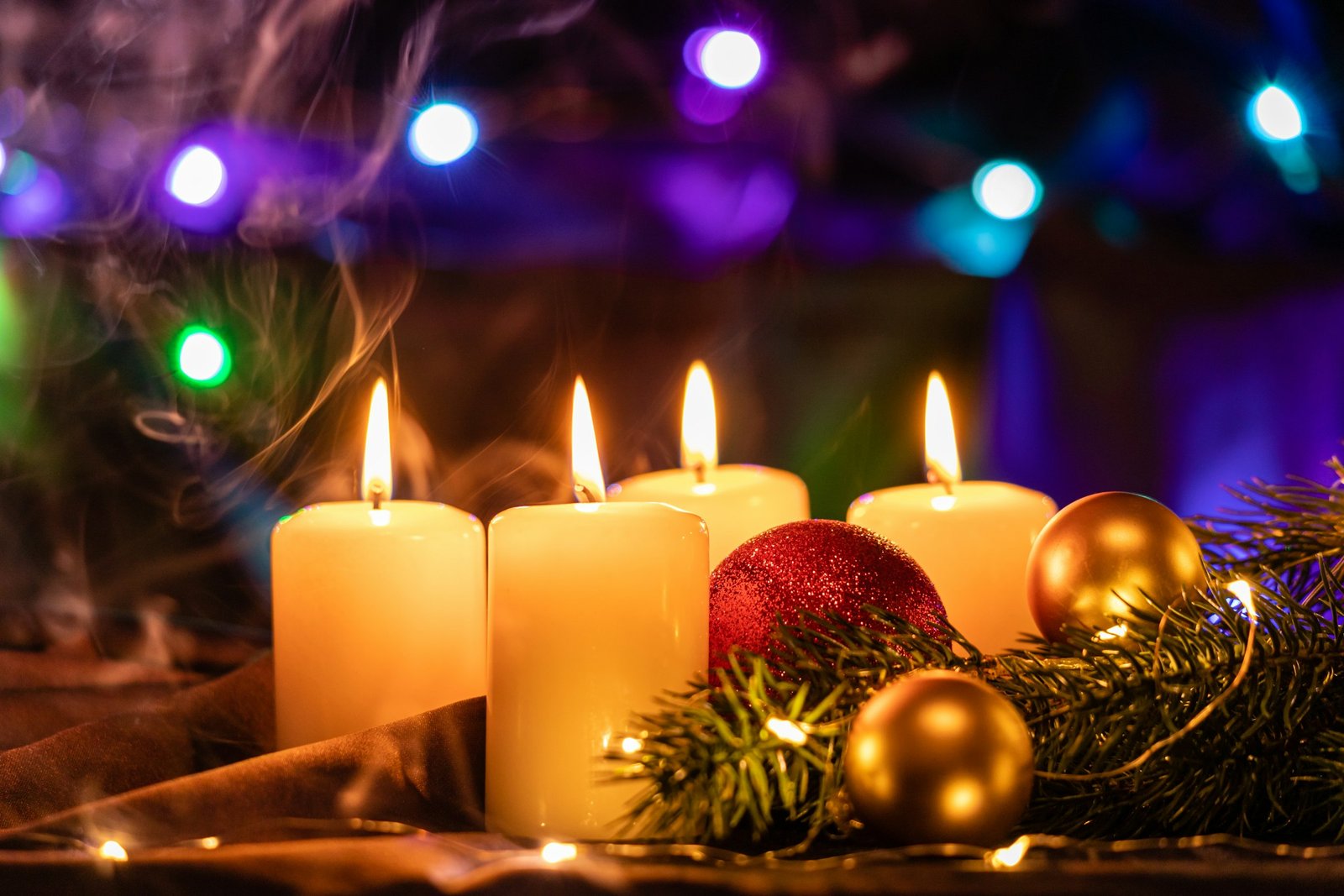 Candle gift ideas: lit ivory pillar candles with gold ornaments and pine on a holiday table