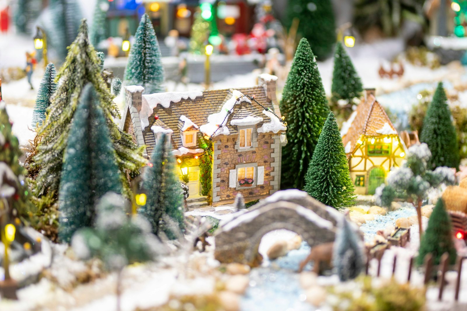 Ceramic Christmas village idea: lighted miniature houses, snowy bridge and bottle brush trees in a holiday display